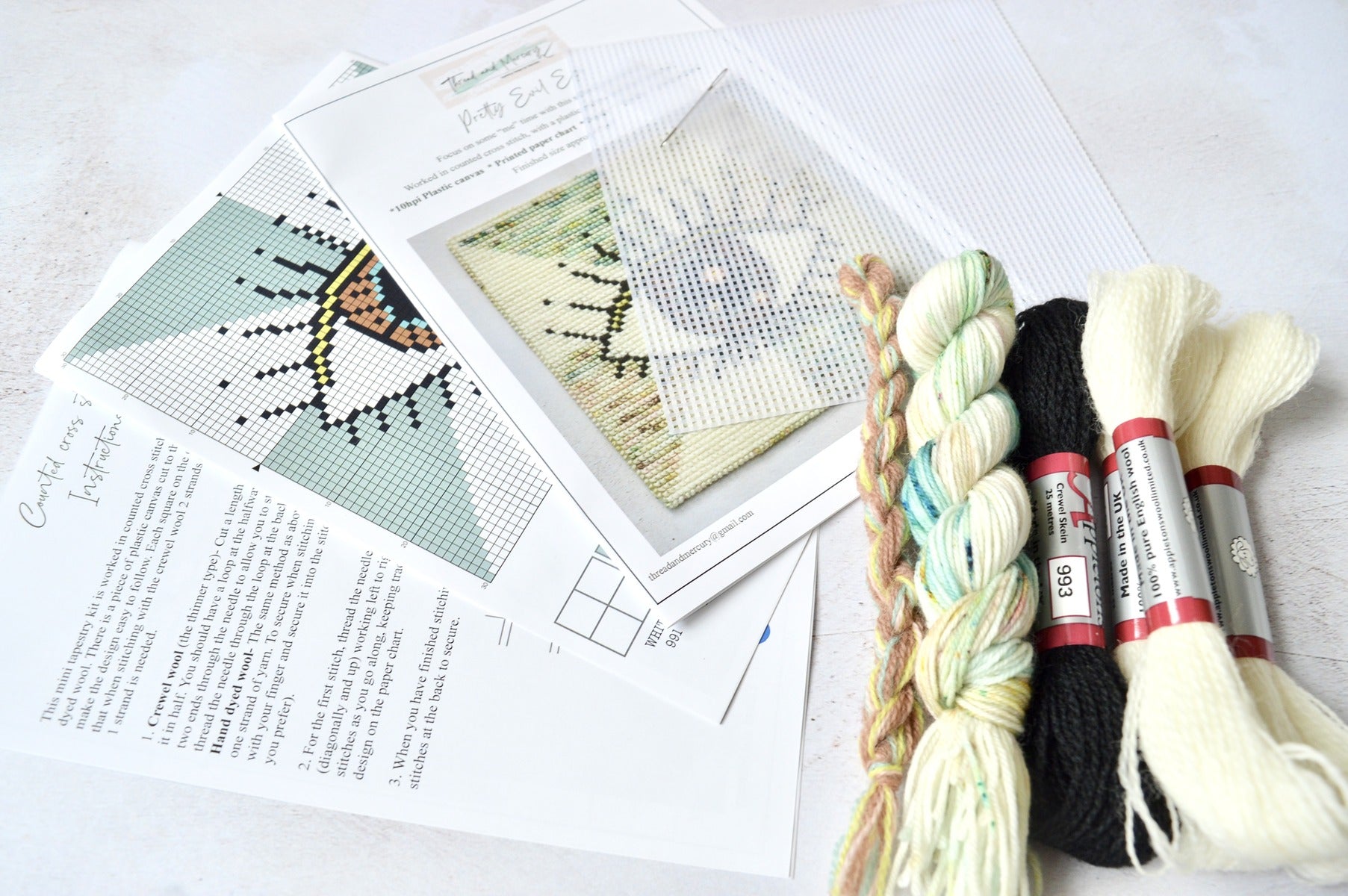 An image of an evil eye tapestry kit, featuring a combination of wool and hand-dyed yarn. The kit includes materials for stitching the intricate design of the evil eye motif, incorporating rich hues and textures. Perfect for craft enthusiasts looking to create a unique and protective piece of art for their space.