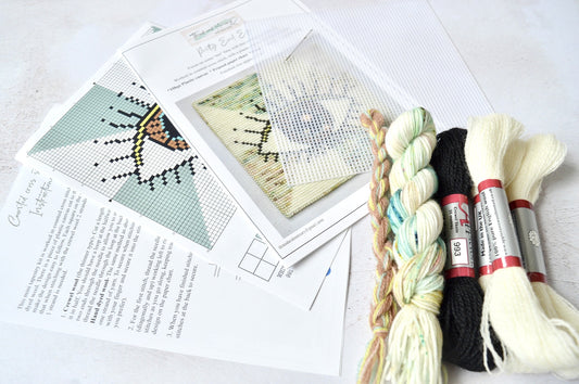 An image of an evil eye tapestry kit, featuring a combination of wool and hand-dyed yarn. The kit includes materials for stitching the intricate design of the evil eye motif, incorporating rich hues and textures. Perfect for craft enthusiasts looking to create a unique and protective piece of art for their space.
