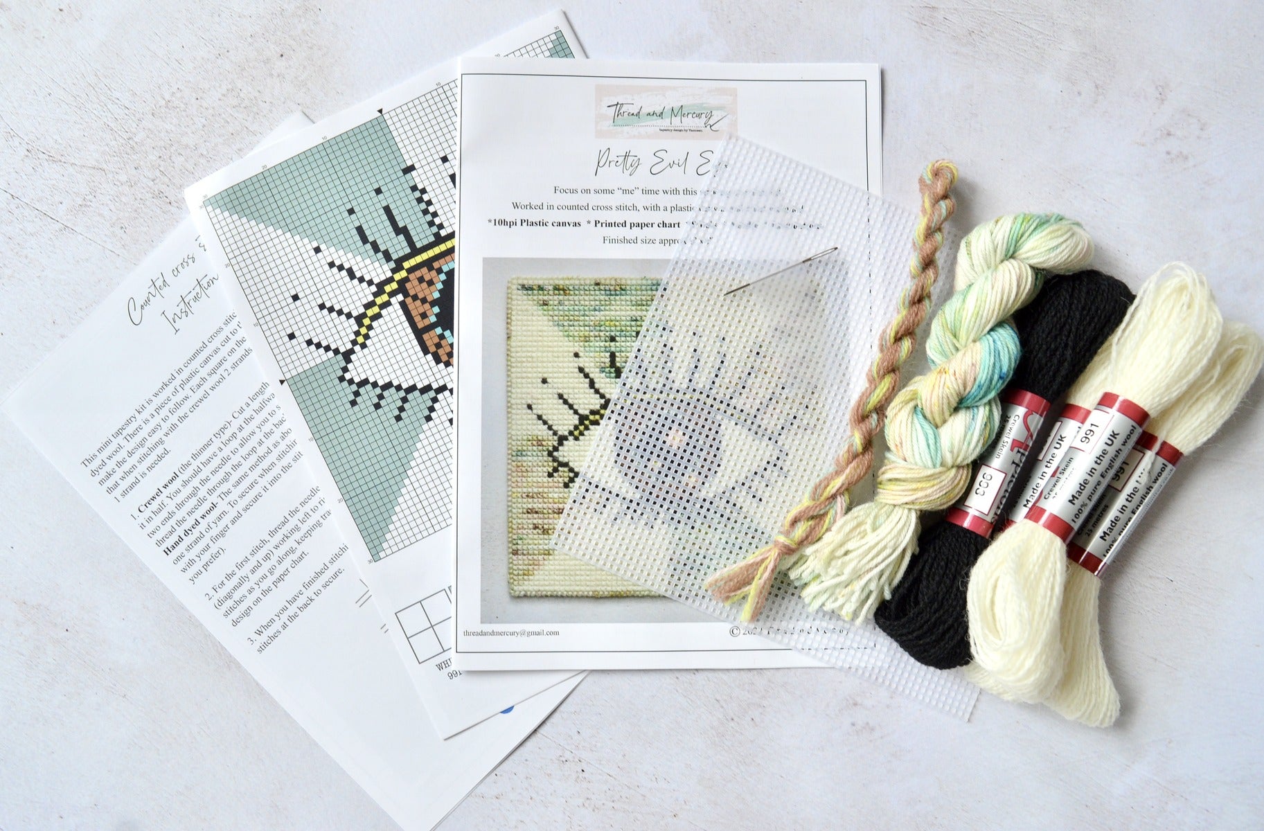 An image of an evil eye tapestry kit designed for cross-stitching onto plastic canvas. The kit includes all necessary materials, such as wool and a plastic canvas