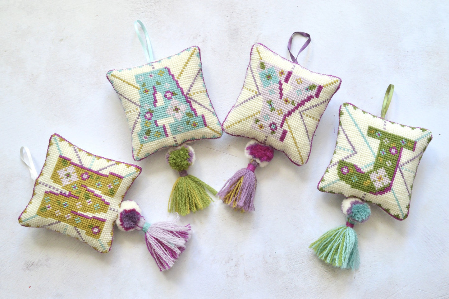 Colourful tapestry letter decorations created using cross stitching and wool. Finished with pom poms and tassles.