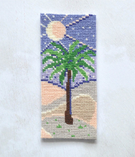 cross stitch bookmark of a palm tree in the desert with the night sky. Design available to buy as a downloadable cross stitch chart
