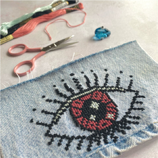 a downloadable pdf of an iconic evil eye design cross stitched onto denim using stranded cotton