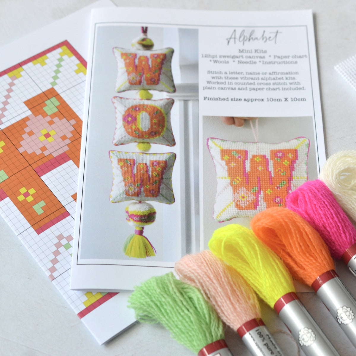 An image of an alphabet mini kit showing the contents, which includes skeins of appletons crewel wool, a printed paper chart and an instruction leaflet.