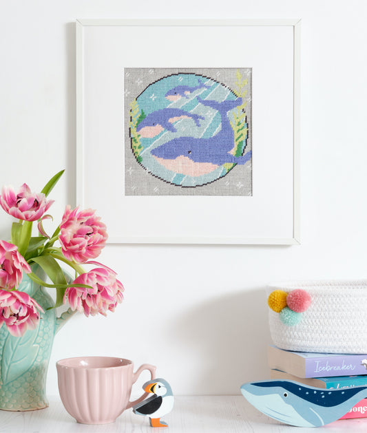 The finished whale tapestry kit hanging on a wall, featuring 3 whales swimming gracefully in a deep blue ocean, surrounded by other marine life , stitched with intricate details and various shades of blue and green thread.
