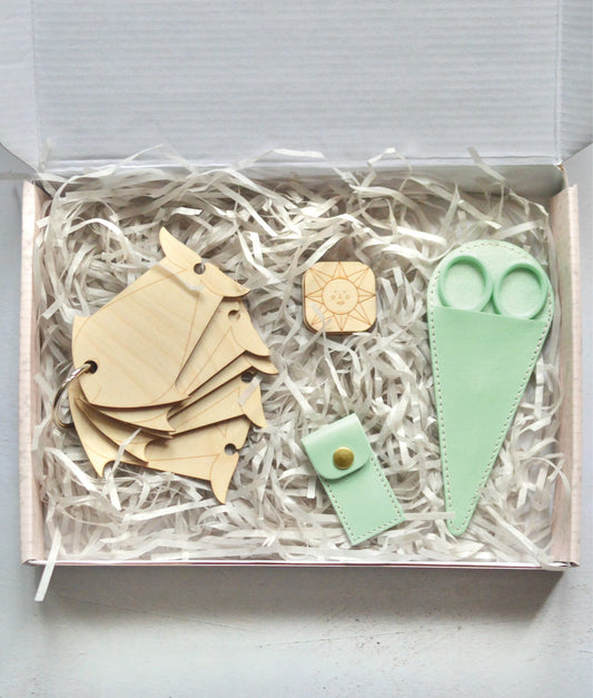 A gift box for tapestry enthusiasts containing yarn bobbins, needle minder, tapestry needles and case, and scissors with a case.