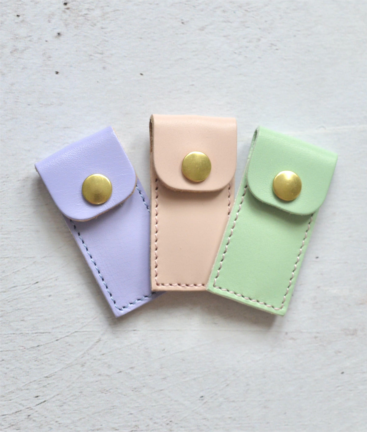 pastel coloured leather cases to hold tapestry needles. Colours include lilac, pink and mint green.