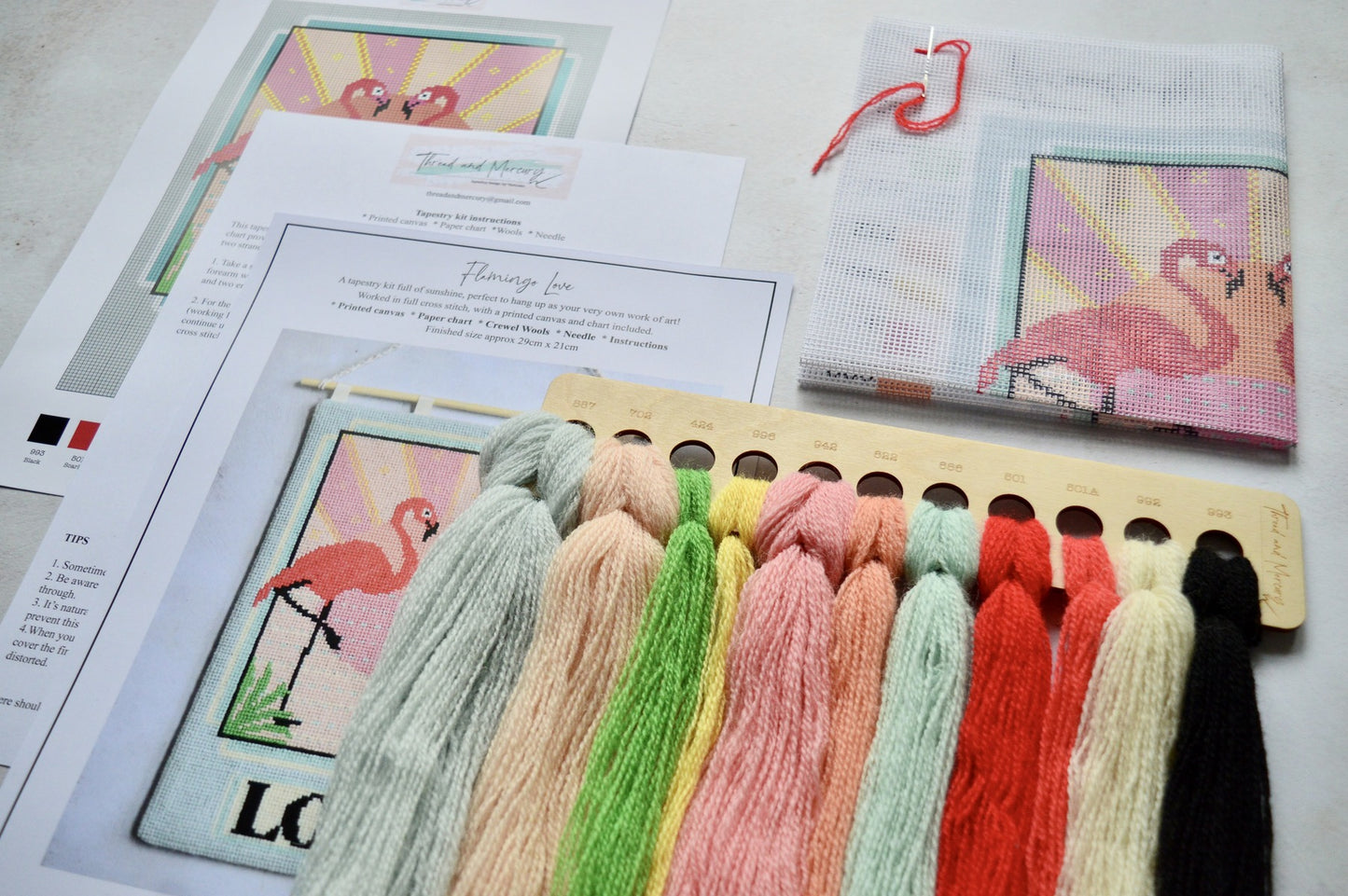 An image of a tapestry kit with wool threads and a printed canvas. The canvas depicts a flamingo design ready for stitching. The kit provides all necessary materials for creating a textured and colourful tapestry masterpiece